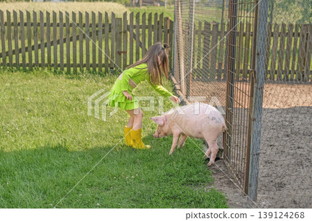 A girl strokes a little piglet walking around the courtyard. Love for animals since childhood 139124268
