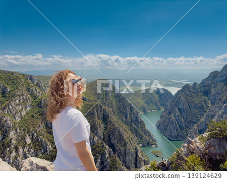 Hiker woman on the background of a mountain river. Girl traveler stands on the edge of rock 139124629