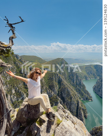 Hiker woman on the background of a mountain river. Girl traveler stands on the edge of rock Hiker woman on the background of a mountain river. Girl traveler stands on the edge of rock 139124630