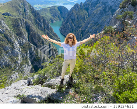 Hiker woman on the background of a mountain river. Girl traveler stands on the edge of rock Hiker woman on the background of a mountain river. Girl traveler stands on the edge of rock 139124631