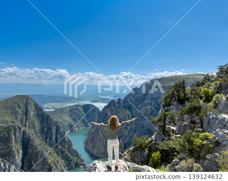 Hiker woman on the background of a mountain river. Girl traveler stands on the edge of rock Hiker woman on the background of a mountain river. Girl traveler stands on the edge of rock 139124632