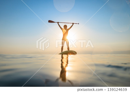 Silhouette of girl walking on sup board by the sea during summer vacation Silhouette of girl walking on sup board by the sea during summer vacation 139124639
