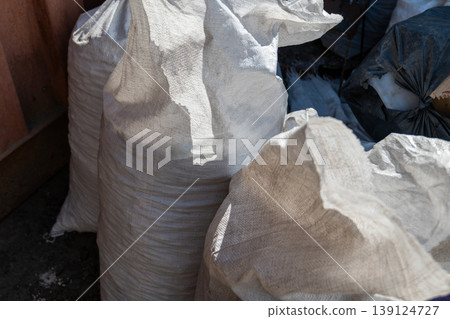 Sunlight dances on the textured surface of white sacks, stacked in a narrow alleyway by a busy construction site, hinting at ongoing projects Sunlight dances on the textured surface of white sacks, stacked in a narrow alleyway by a busy construction site, hinting at ongoing projects 139124727