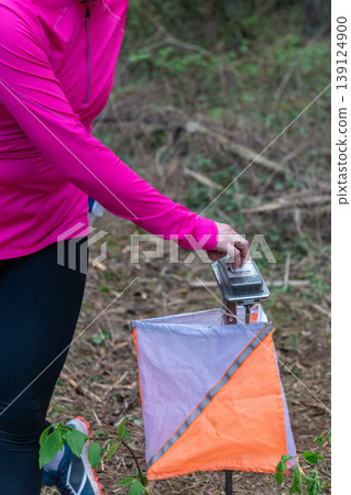 Athlete punches electronic timing device at orienteering control point 139124900