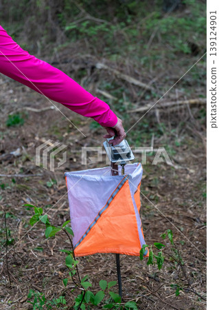 Athlete punches electronic timing device at orienteering control point 139124901