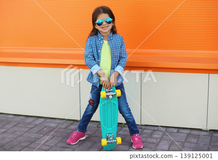 Stylish girl child with skateboard posing in the city Stylish girl child with skateboard posing in the city 139125001