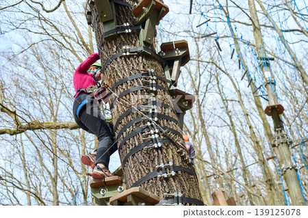 Person in helmet and harness climbing tree obstacle with wooden platforms in adventure park Person in helmet and harness climbing tree obstacle with wooden platforms in adventure park 139125078
