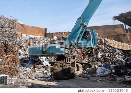 Excavator loading scrap metal onto truck in junkyard. Excavator loading scrap metal onto truck in junkyard. 139125943