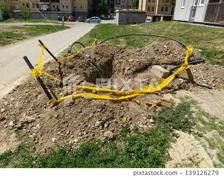 Sremska Mitrovica, Serbia, May 9, 2020. A hole dug in the lawn is surrounded by a warning tape. Repair and earthworks. Construction and installation of pipes and cables Sremska Mitrovica, Serbia, May 9, 2020. A hole dug in the lawn is surrounded by a warning tape. Repair and earthworks. Construction and installation of pipes and cables 139126279