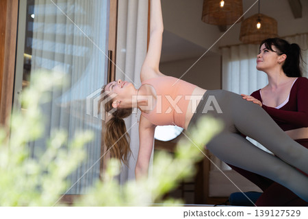 Young woman doing side plank yoga pose with personal trainer at home 139127529