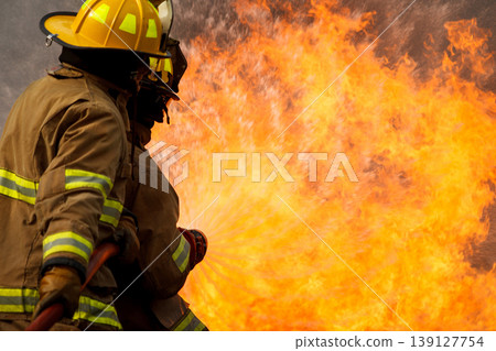 Professional fire fighters extinguishing intense fire with water hose Professional fire fighters extinguishing intense fire with water hose 139127754