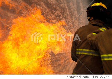 Professional fire fighters extinguishing intense fire with water hose Professional fire fighters extinguishing intense fire with water hose 139127756