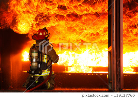 Professional fire fighter extinguishing blazing fire during emergency Professional fire fighter extinguishing blazing fire during emergency 139127760