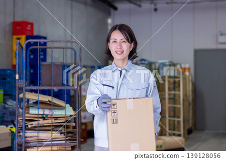 A woman carrying cardboard boxes in a warehouse. A woman carrying cardboard boxes in a warehouse. 139128056