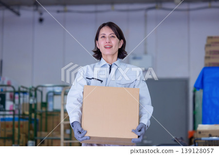A woman carrying cardboard boxes in a warehouse. 139128057