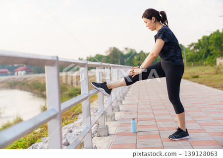 Asian woman in sportswear stretching her leg on park fence Asian woman in sportswear stretching her leg on park fence 139128063