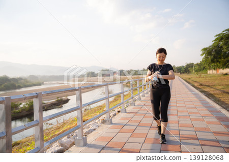 Active Asian female looking at fitness tracker during outdoor exercise Active Asian female looking at fitness tracker during outdoor exercise 139128068