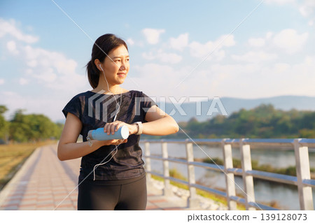 Active Asian female looking at fitness tracker during outdoor exercise Active Asian female looking at fitness tracker during outdoor exercise 139128073