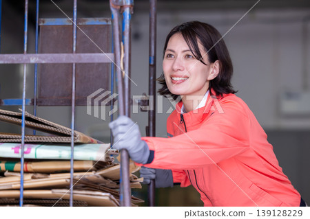 一名女子在倉庫裡推著一輛紙板車。 139128229
