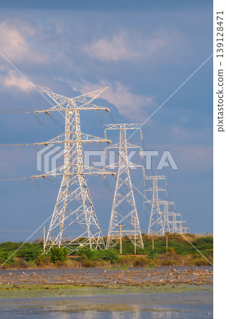 High voltage power transmission towers across coastal wetland landscape in Mannar, Sri Lanka, under a dramatic blue sky High voltage power transmission towers across coastal wetland landscape in Mannar, Sri Lanka, under a dramatic blue sky 139128471