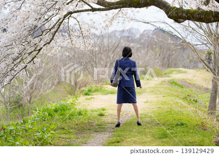 The back view of a woman in a suit standing defiantly under a cherry tree. The back view of a woman in a suit standing defiantly under a cherry tree. 139129429