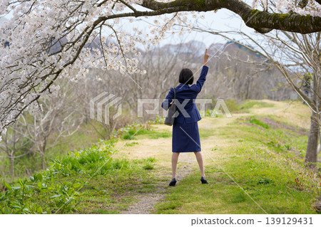 The back view of a woman in a suit raising her hand under a cherry tree. The back view of a woman in a suit raising her hand under a cherry tree. 139129431