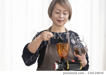 一位老婦人在客廳磨咖啡豆,然後喝咖啡。 一位老婦人在客廳磨咖啡豆,然後喝咖啡。 139129649