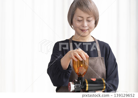 A senior woman grinds coffee beans and drinks coffee in her living room. A senior woman grinds coffee beans and drinks coffee in her living room. 139129652