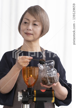 A senior woman grinds coffee beans and drinks coffee in her living room. 139129659