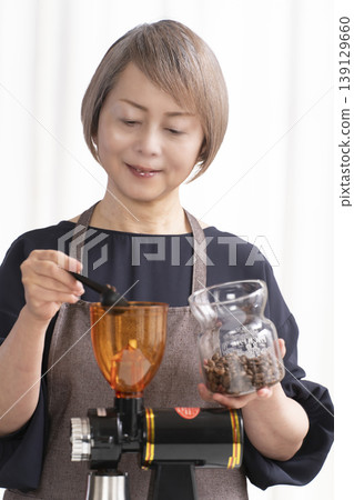 A senior woman grinds coffee beans and drinks coffee in her living room. A senior woman grinds coffee beans and drinks coffee in her living room. 139129660