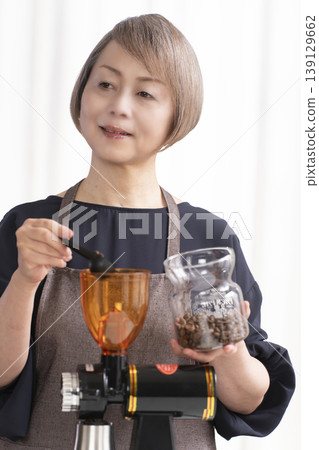 A senior woman grinds coffee beans and drinks coffee in her living room. 139129662