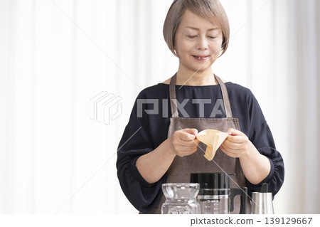 A senior woman grinds coffee beans and drinks coffee in her living room. 139129667