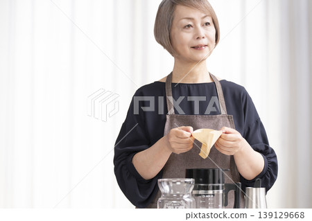 一位老婦人在客廳磨咖啡豆,然後喝咖啡。 一位老婦人在客廳磨咖啡豆,然後喝咖啡。 139129668