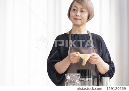 一位老婦人在客廳磨咖啡豆，然後喝咖啡。 139129669