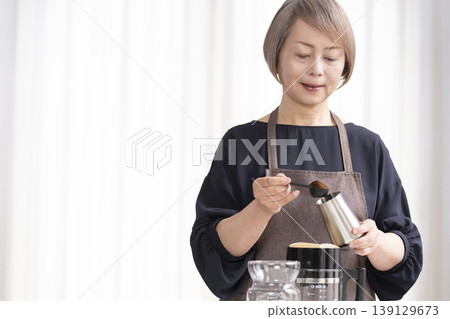一位老婦人在客廳磨咖啡豆,然後喝咖啡。 一位老婦人在客廳磨咖啡豆,然後喝咖啡。 139129673