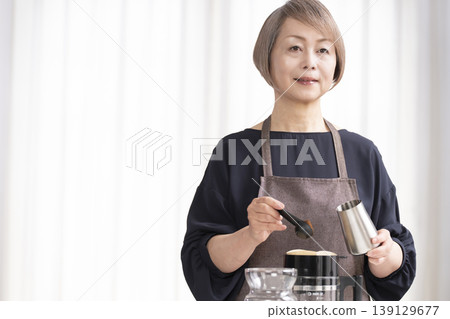 A senior woman grinds coffee beans and drinks coffee in her living room. A senior woman grinds coffee beans and drinks coffee in her living room. 139129677