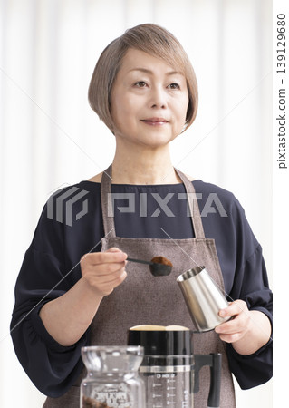 A senior woman grinds coffee beans and drinks coffee in her living room. A senior woman grinds coffee beans and drinks coffee in her living room. 139129680