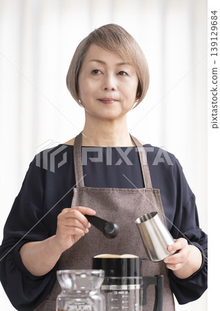 一位老婦人在客廳磨咖啡豆,然後喝咖啡。 一位老婦人在客廳磨咖啡豆,然後喝咖啡。 139129684