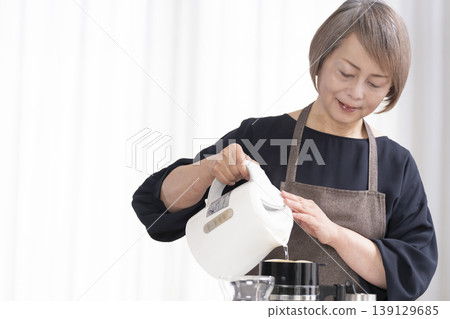 一位老婦人在客廳磨咖啡豆,然後喝咖啡。 一位老婦人在客廳磨咖啡豆,然後喝咖啡。 139129685