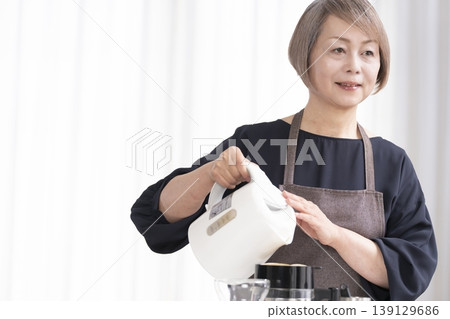 一位老婦人在客廳磨咖啡豆,然後喝咖啡。 一位老婦人在客廳磨咖啡豆,然後喝咖啡。 139129686