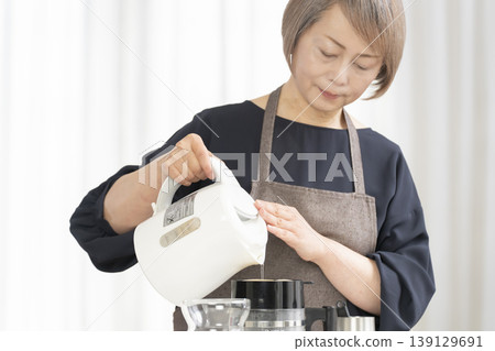 一位老婦人在客廳磨咖啡豆，然後喝咖啡。 139129691