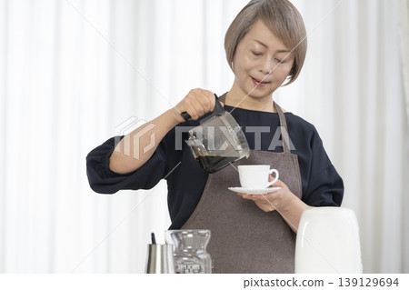 A senior woman grinds coffee beans and drinks coffee in her living room. 139129694