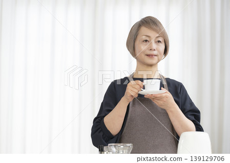 一位老婦人在客廳磨咖啡豆，然後喝咖啡。 139129706
