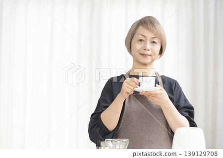 一位老婦人在客廳磨咖啡豆，然後喝咖啡。 139129708