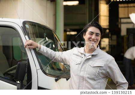 一位工人站在輕型卡車旁，微笑地看著鏡頭；主題可能包括司機職業轉型或製造業的送貨工作。 139130215