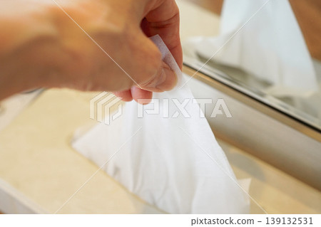 A hand taking tissue paper from a box on the bathroom counter. A hand taking tissue paper from a box on the bathroom counter. 139132531