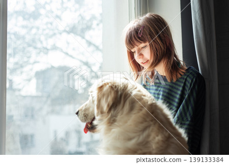 Girl and golden retriever looking out window 139133384
