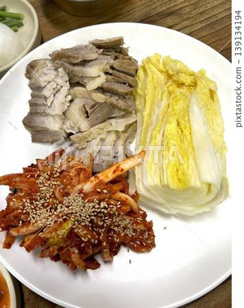 Tender slices of bossam, Korean boiled pork belly, served with fresh lettuce, garlic, and ssamjang. This flavorful and savory dish is perfect for wrapping and sharing in a traditional Korean meal. Tender slices of bossam, Korean boiled pork belly, served with fresh lettuce, garlic, and ssamjang. This flavorful and savory dish is perfect for wrapping and sharing in a traditional Korean meal. 139134194