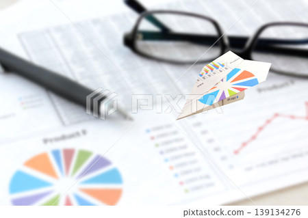 A paper airplane flying over a document with business charts – an image of flying data. A paper airplane flying over a document with business charts – an image of flying data. 139134276