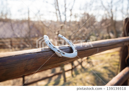 Metal horseshoe placed on a wooden railing in a zoo environment with blurred trees and sunlight in background. Symbol, luck, object Metal horseshoe placed on a wooden railing in a zoo environment with blurred trees and sunlight in background. Symbol, luck, object 139139318